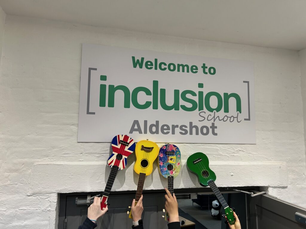 Image for four Ukulele's in front of the Inclusion School Aldershot sign